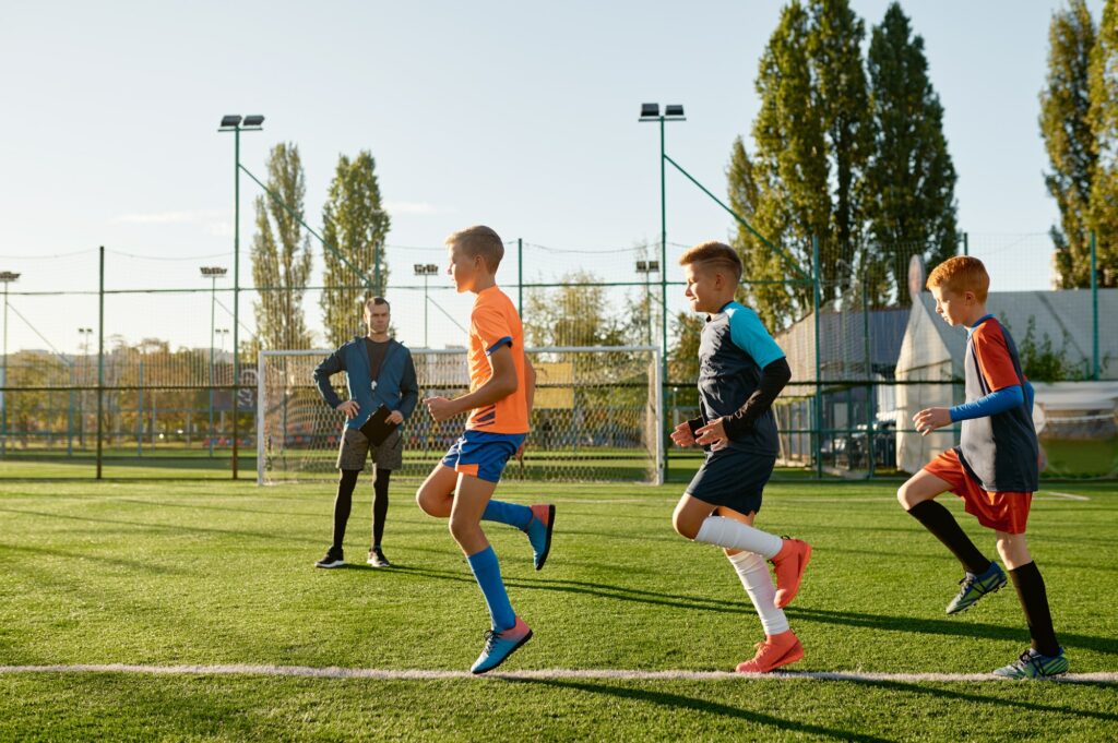 Kids practicing soccer on grass field under football coach control