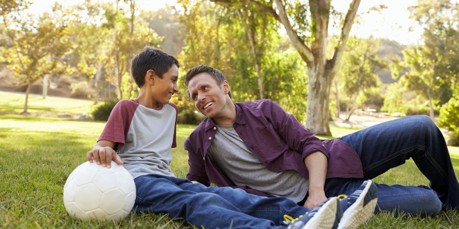 Father and son relaxing with soccer ball in a park, close up