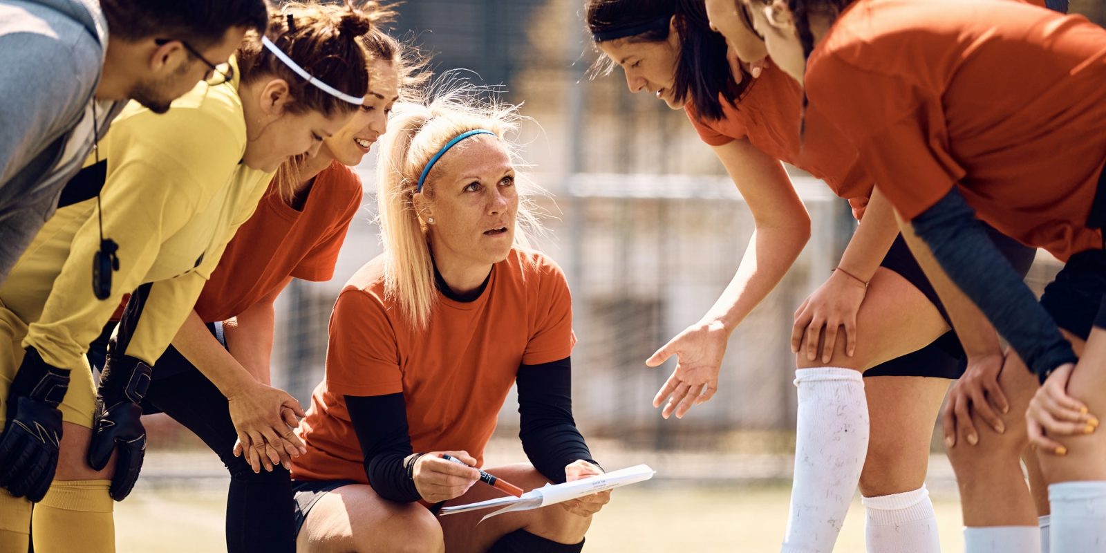 Female soccer team and their coach going through game plan on football pitch.