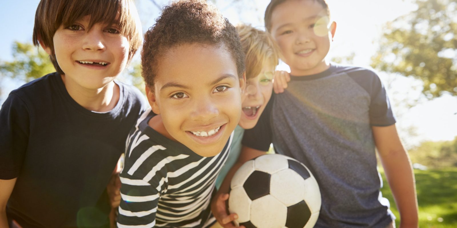 Four young schoolboys leaning in to camera holding football