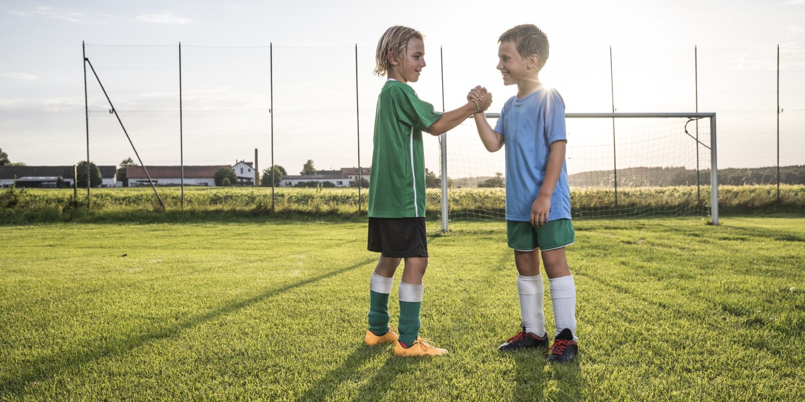 Smiling young football players shaking hands on football ground