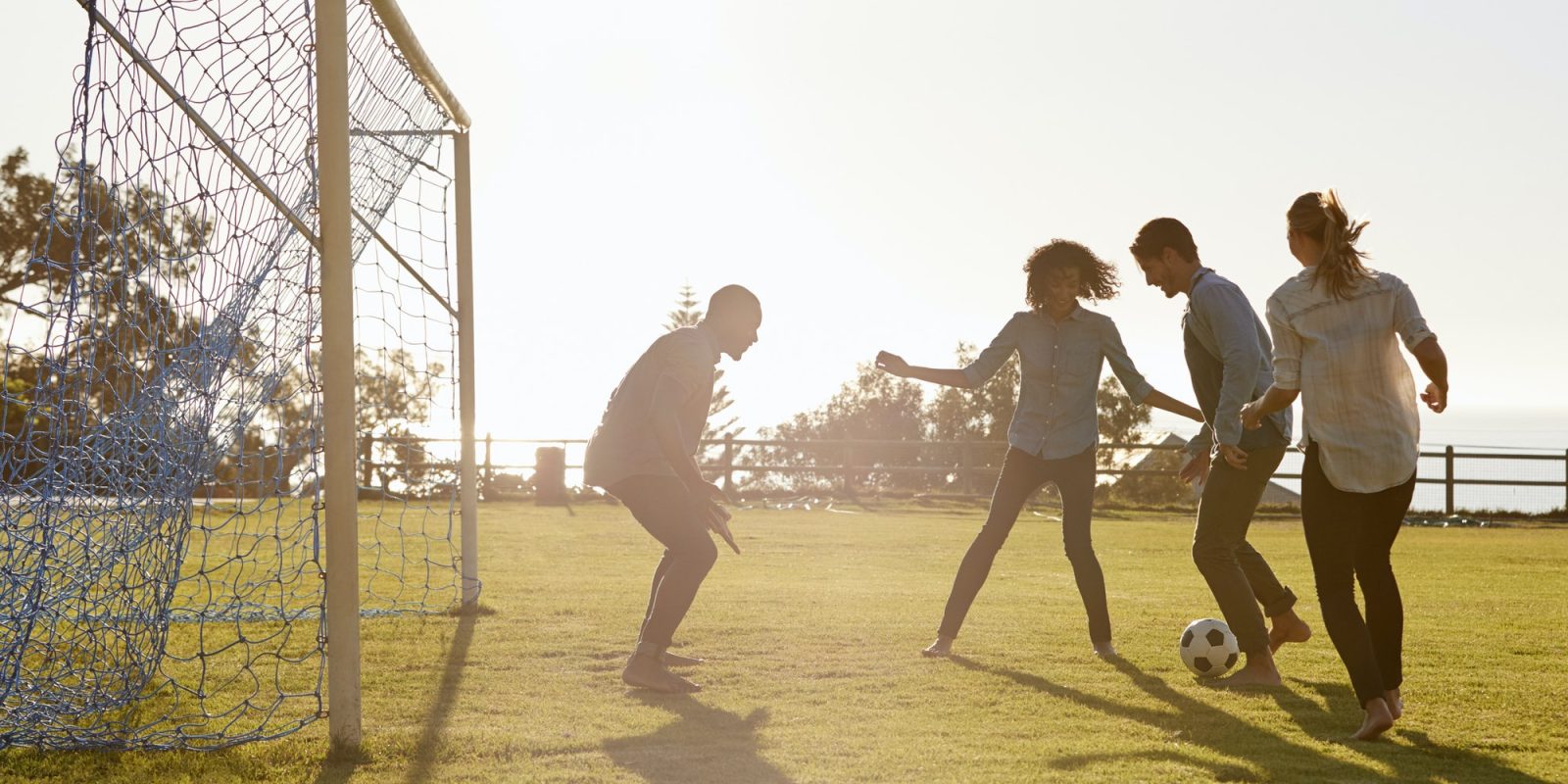 Young adults playing football in park one in goal, side view